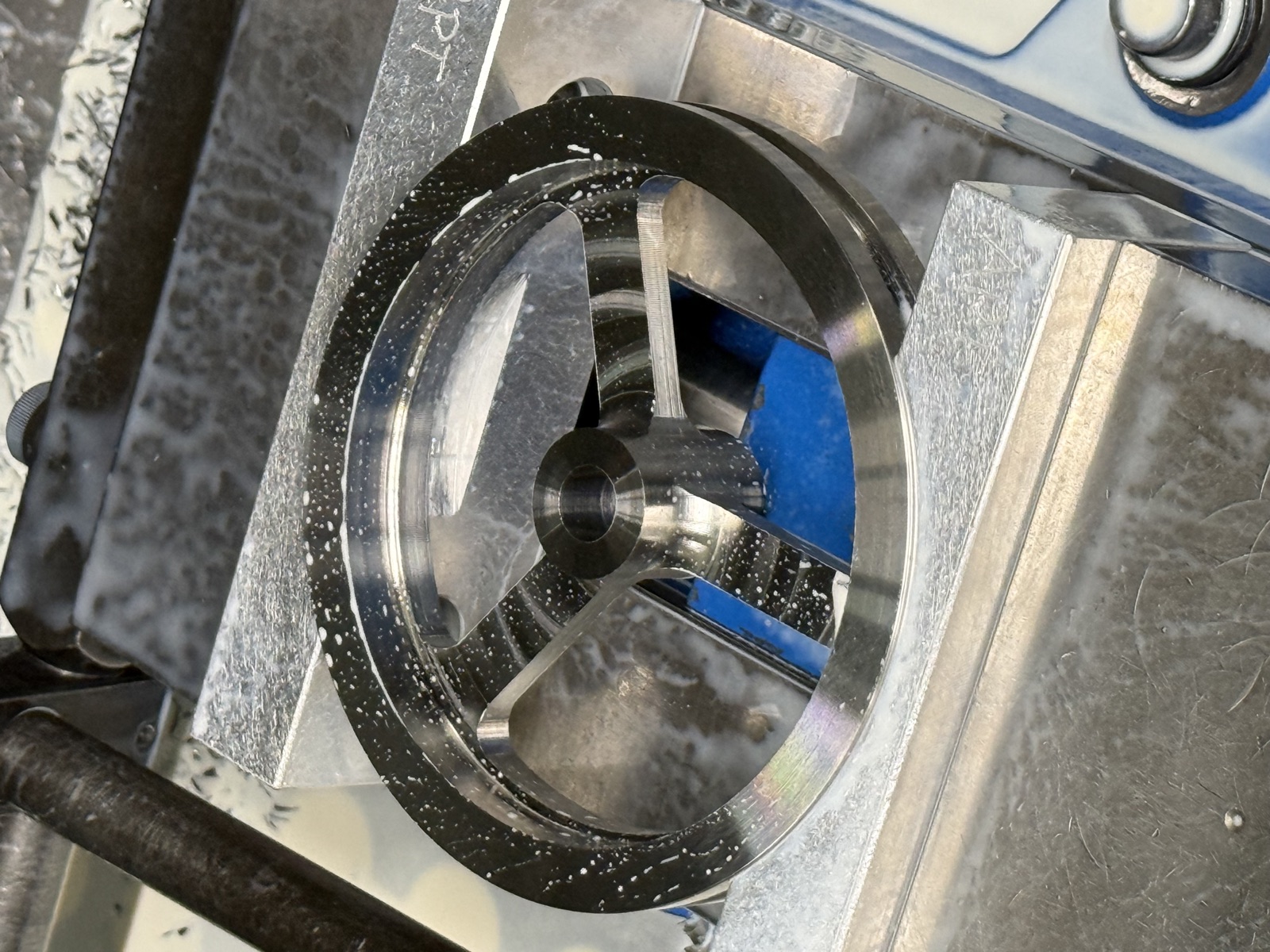 A three-spoke stainless pulley held in aluminum soft jaws in the mill vise, fresh from machining